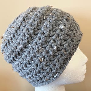 May include: A gray crocheted beanie with white and brown flecks. The beanie is made with a chunky yarn and has a slouchy fit.
