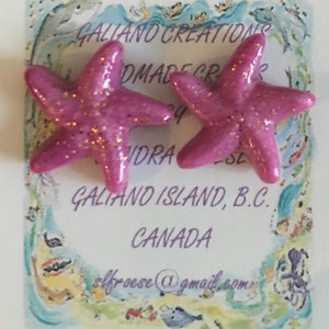 Op de afbeelding: Een paar roze zeestervormige oorbellen met gouden glitteraccenten. De oorbellen worden gepresenteerd op een kaart met de tekst "Galiano Creations Handmade Creations" en de locatie "Galiano Island, B.C., Canada."