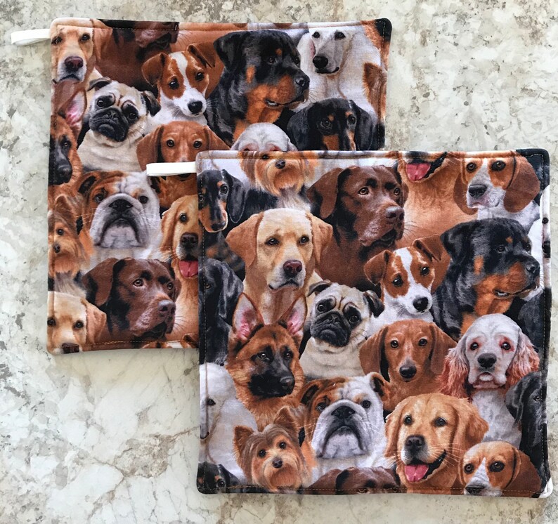 May include: Two brown and beige pot holders with a pattern of various dog breeds. The pot holders are made of fabric and have a white loop for hanging.