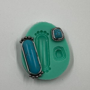 May include: A light green silicone mold with three cavities for jewelry making. The mold contains three silver-toned bezels with turquoise-colored stones. The mold has a footprint design.