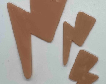May include: Three tan-colored lightning bolt shapes of varying sizes are arranged on a white surface. The largest bolt is at the top, with two smaller bolts below. The shapes have rounded edges.