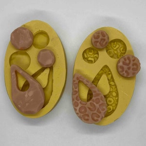 May include: Two yellow silicone molds with various shapes for jewelry making. One mold has a teardrop shape and two round shapes. The other mold has a teardrop shape with a leopard print design and three round shapes.