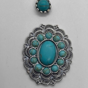 May include: Two pieces of jewelry with turquoise-colored stones. One is a small, round stud. The other is an oval pendant with a silver-colored filigree design and a large turquoise stone in the center, surrounded by smaller turquoise stones.
