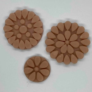 May include: Three beige, circular decorative pieces with a floral design. Each piece features a central circle surrounded by teardrop-shaped elements. The pieces vary in size, with the largest approximately 3 inches in diameter.