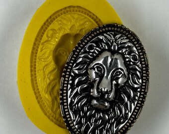 May include: An oval-shaped, silver-colored lion head pendant with a detailed mane and a decorative border. Next to it is a bright yellow silicone mold in the shape of the lion's head. The pendant is likely for jewelry making or crafting.