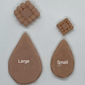 May include: Two pairs of handmade clay earrings in a neutral beige color. One pair is teardrop-shaped, labeled "Large" and "Small". The other pair is square with a central square surrounded by small spheres.