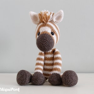 May include: A crocheted zebra stuffed animal with brown and white stripes. The zebra is sitting on a white surface.