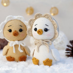 May include: Two crocheted ducklings with black eyes and pink cheeks. The left duckling is light brown with a white bonnet, and the right duckling is white with a beige bonnet. Both have orange feet and beaks. The text ChiquiPork is in the corner.