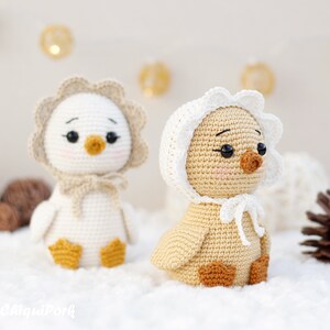 May include: Two crocheted ducklings with black bead eyes and pink cheeks. The left duckling is white with a beige bonnet, and the right duckling is light brown with a white bonnet. Both have orange feet and beaks, and the text "ChiquiPork" is visible.