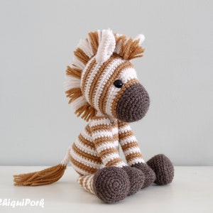 May include: A crocheted zebra stuffed animal with brown and white stripes. The zebra is sitting with its legs crossed and has a brown tail and mane.