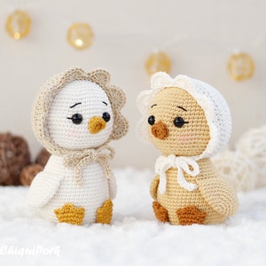 May include: Two crocheted ducklings with black bead eyes and pink cheeks. The left duckling is white with a beige bonnet and yellow feet. The right duckling is light brown with a white bonnet and brown feet. Both have small orange beaks.