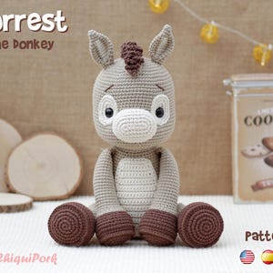 May include: A crocheted donkey toy in shades of beige and brown, with the text "Forrest the donkey" at the top. The toy has large eyes and a detailed mane. The word "Pattern" is at the bottom, along with flags.
