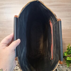 May include: Vintage handbag with a woven exterior and black interior. The bag features a rectangular shape with a black handle and a red zipper. The bag is held open, revealing the interior.