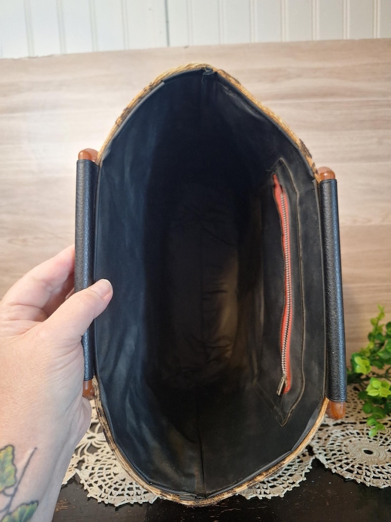 May include: Vintage handbag with a woven exterior and black interior. The bag features a rectangular shape with a black handle and a red zipper. The bag is held open, revealing the interior.