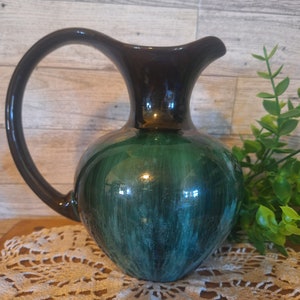 May include: A green and black ceramic pitcher with a wide mouth and a curved handle. The pitcher has a glossy finish and a streaky green glaze.