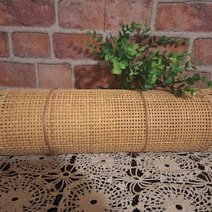 May include: A close-up of a woven cane roll with a natural brown color. The roll is on a white crocheted surface.