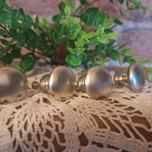 May include: Four silver-toned cabinet knobs with a round, slightly domed shape. The knobs are arranged in a row on a white crocheted doily.