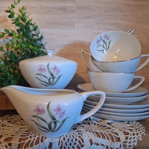 May include: A white tea set with a floral design. The set includes a creamer, sugar bowl, and four teacups and saucers. The cups and saucers are stacked on top of each other.