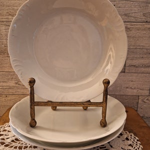 May include: Two white ceramic bowls with scalloped edges are displayed on a gold metal stand. The bowls are stacked on top of each other and are sitting on a white crocheted doily.