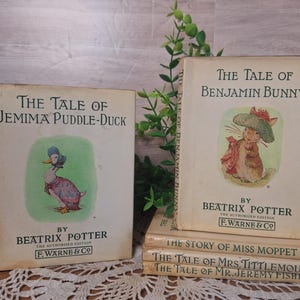 May include: Two vintage children's books by Beatrix Potter. "The Tale of Jemima Puddle-Duck" features a duck illustration, while "The Tale of Benjamin Bunny" shows a rabbit. Additional titles are stacked below, including "The Story of Miss Moppet".