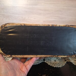 May include: A rectangular basket with a black bottom and woven sides. The basket is held by a person's hand. The basket's sides are a light brown color with dark brown accents. The bottom is a solid black material.