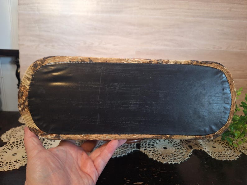 May include: A rectangular basket with a black bottom and woven sides. The basket is held by a person's hand. The basket's sides are a light brown color with dark brown accents. The bottom is a solid black material.