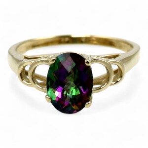 May include: A gold ring with an oval-shaped, multi-colored gemstone. The gemstone has shades of green, purple, and red. The ring has a delicate, twisted band.