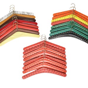 May include: A stack of colourful leather-covered hangers with gold metal hooks. The hangers are in various shades of red, orange, yellow, green, and black. Some of the hangers have a studded design.