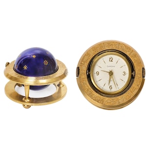 May include: Two antique decorative items: a brass globe with a dark blue sphere adorned with gold starbursts, and a Europa-branded clock in a brass case. The clock face is white with black numerals.