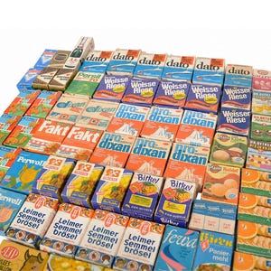 Può includere: Una vasta collezione di scatole rettangolari vintage in cartone per prodotti alimentari e per la casa, disposte a griglia. Le scatole presentano vari marchi tra cui Dato, Weisse Riese, Pro-Dixan, Perwoll, Leimer Semmel Brösel e Dr. Oetker, con design grafici colorati e testo.