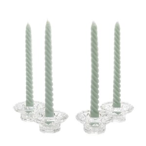 Peut inclure: Ensemble de quatre bougeoirs en verre transparent avec quatre bougies torsadées. Les bougies sont de couleur vert sauge clair.