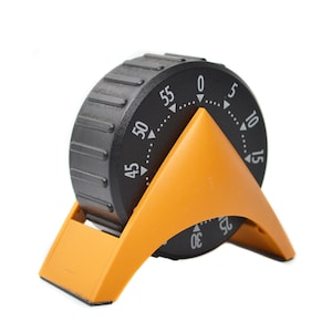 May include: A black and orange kitchen timer with a dial showing numbers from 0 to 55 minutes. The timer has an orange stand and a black dial with white markings.
