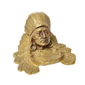 Op de afbeelding: Een gouden messing inktpot in de vorm van een Indiaans opperhoofd met een verenhoed. De inktpot heeft een klein, rond, open bovendeel om inkt in te bewaren.