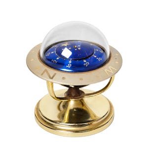 Op de afbeelding: Een nautisch kompas van messing met een blauwe wijzerplaat, gouden stermotieven en numerieke markeringen onder een heldere glazen koepel. Het kompas is gemonteerd op een ronde messing voet met een cardanische ring en toont de letters N en W.
