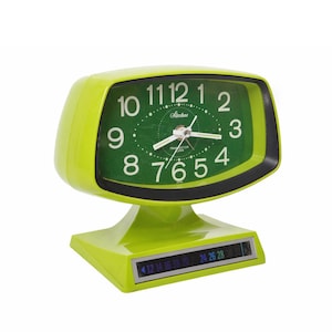 May include: A lime green vintage alarm clock with a green face and white numerals. The clock face has the brand name "Sinstone" and the word "TRANSISTOR" printed on it. The clock also has a date display.