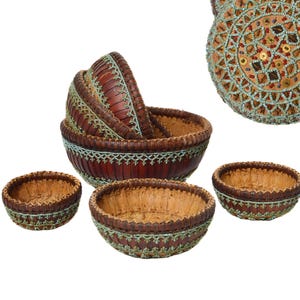 Op de afbeelding: Een set decoratieve bruin geweven manden met een lichtbruin interieur. De randen zijn versierd met een turquoise kralenpatroon. De set bevat verschillende maten, met een deksel zichtbaar in de rechterbovenhoek.