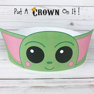 May include: A green and pink paper crown with a cartoon face of a character with large eyes and a small nose. The crown says "Put A Crown On It!" at the top.