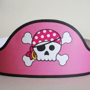 Könnte beinhalten: Rosaer Papier-Piratenhut mit einem weißen Totenkopf- und Knochenkreuz-Design. Der Totenkopf trägt ein rosa-weißes, gepunktetes Bandana mit einem Augenklappen.