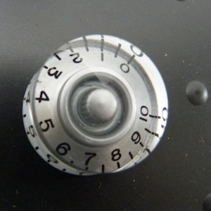 May include: A silver knob with numbers 2 through 10 printed around the edge. The knob is used to adjust a setting.