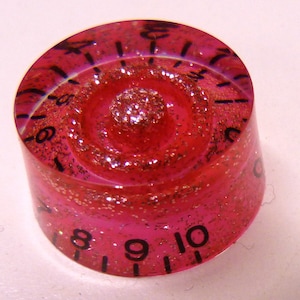 May include: Pink guitar knob with a glittery finish and black numbers from 1 to 10.