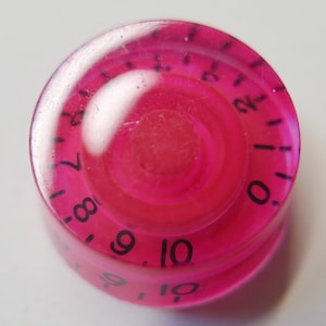 May include: A pink plastic knob with black numbers from 0 to 10. The knob is clear and has a raised centre.