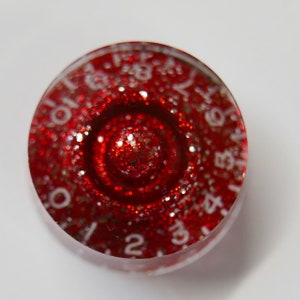 Pode incluir: Um botão redondo de resina transparente vermelha com números brancos de 0 a 9 e uma superfície vermelha brilhante.