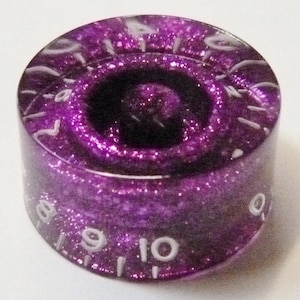 Pode incluir: Botão de guitarra roxo com números brancos de 1 a 10. O botão tem um acabamento brilhante.