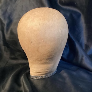 May include: A vintage fabric-covered dressmaker's head form with a metal base. The head form is beige and the base is silver.