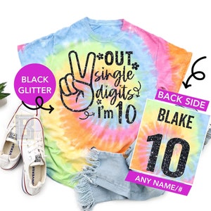 May include: A tie-dye t-shirt with a peace sign and the text "Out single digits I'm 10" in black glitter. The back of the shirt has a black glitter number 10 with the name "Blake" above it. The text "Any name/#" is below the number.