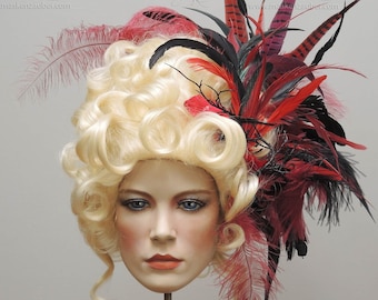 May include: A blonde wig with a large, elaborate feather headdress. The headdress is made of red, black, and white feathers. The wig is styled in a large, curly updo.