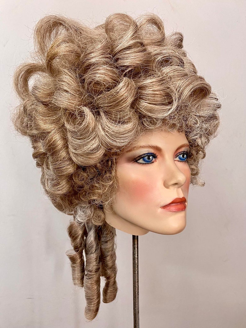 K&ouml;nnte beinhalten: Eine blonde Per&uuml;cke mit gro&szlig;en Locken oben und kleineren Locken im Nacken. Die Per&uuml;cke ist klassisch und elegant gestylt.