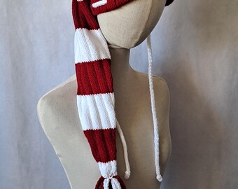 May include: A red and white striped knit hat with a long, dangling tail. The hat has a white pom-pom on top and a white tassel on the end of the tail.