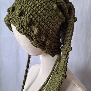 May include: A green crocheted hat with a long, pointed tail. The hat has a textured surface and is made with a bulky yarn.