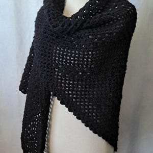 May include: A black crocheted shawl with a lacy pattern and fringe. The shawl is draped over a white mannequin.
